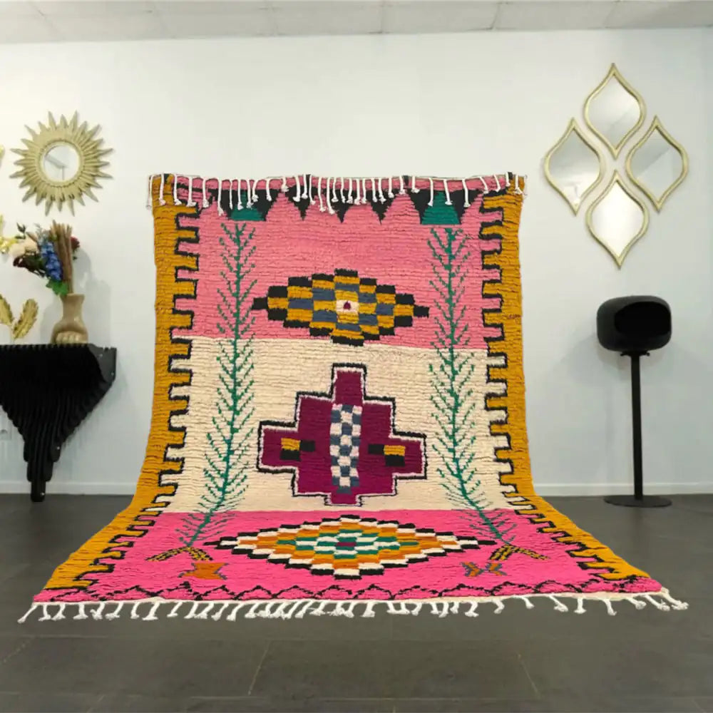 Grand tapis azilal coloré avec motifs géométriques et fond rose, exposé dans un salon moderne marocain