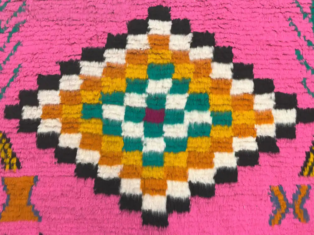 Motif losange multicolore sur fond rose vif d’un tapis azilal tissé main, détails précis