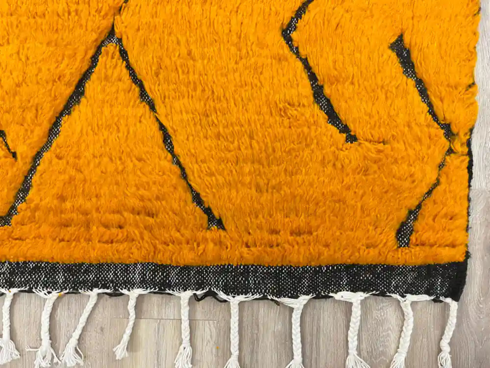 Franges tressées à la main, finition artisanale d’un tapis ethnique en laine naturelle