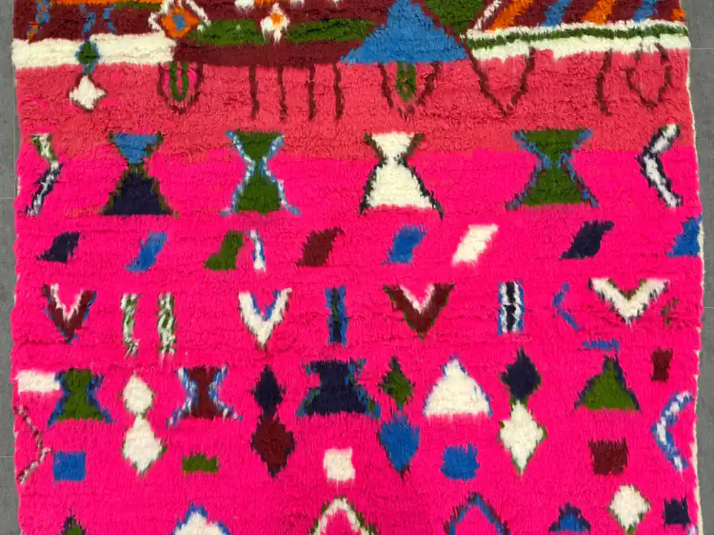 Motif multicolore sur fond rose vif d’un tapis boujaad tissé main, détails précis
