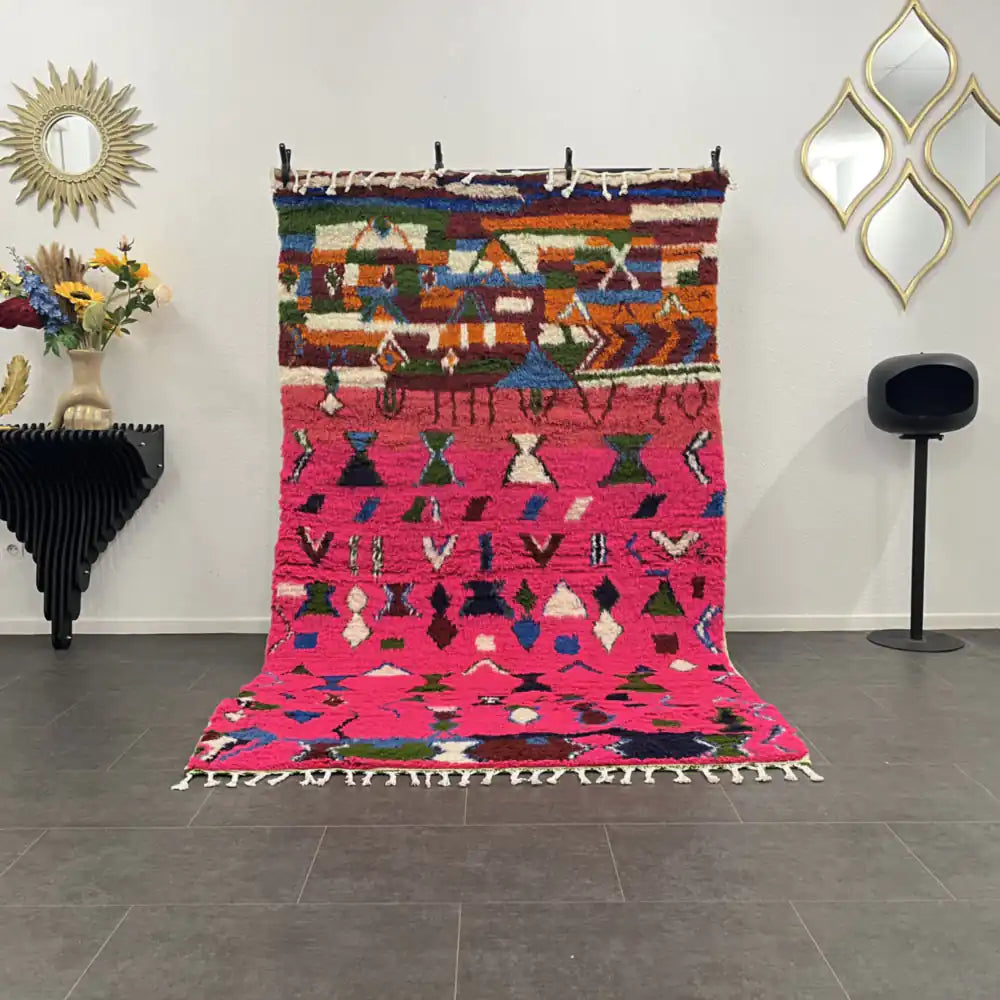 Tapis boujaad  coloré avec motifs géométriques et fond rose, exposé dans un salon moderne marocain