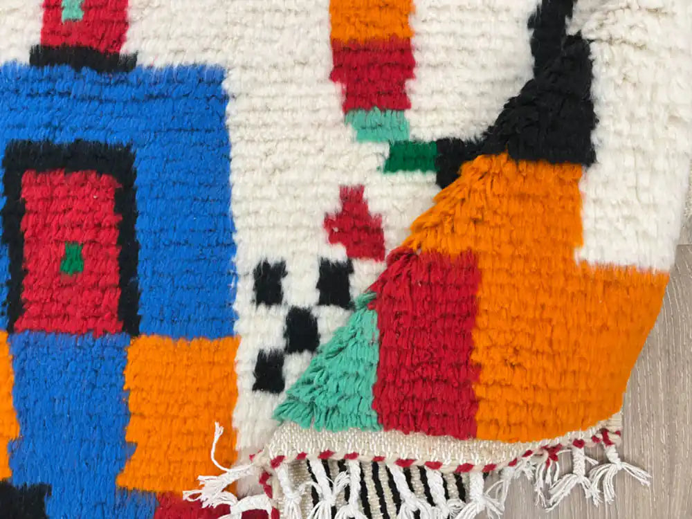 Tapis Azilal plié, mettant en valeur la frange et la texture de la laine naturelle multicolore.