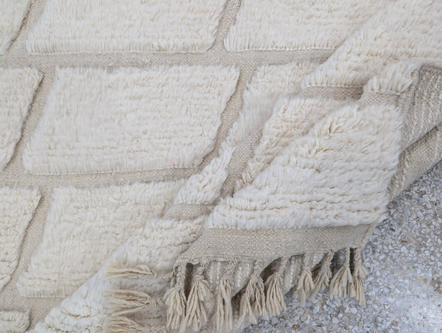 Tapis Beni Ouarain blanc plié sur le côté, mettant en valeur la texture de la laine