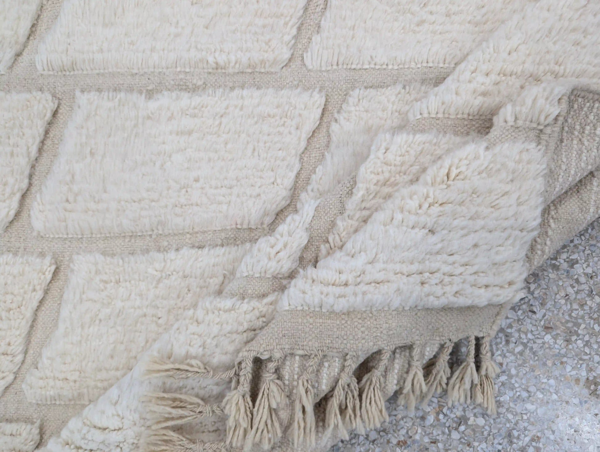 Tapis Beni Ouarain blanc plié sur le côté, mettant en valeur la texture de la laine