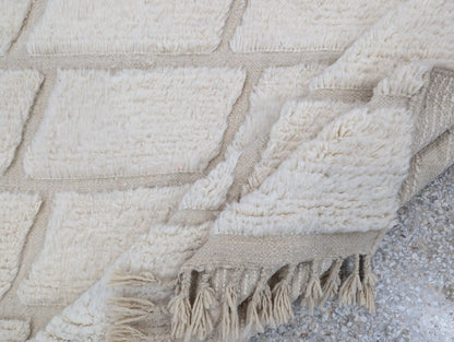 Tapis Beni Ouarain blanc plié sur le côté, mettant en valeur la texture de la laine