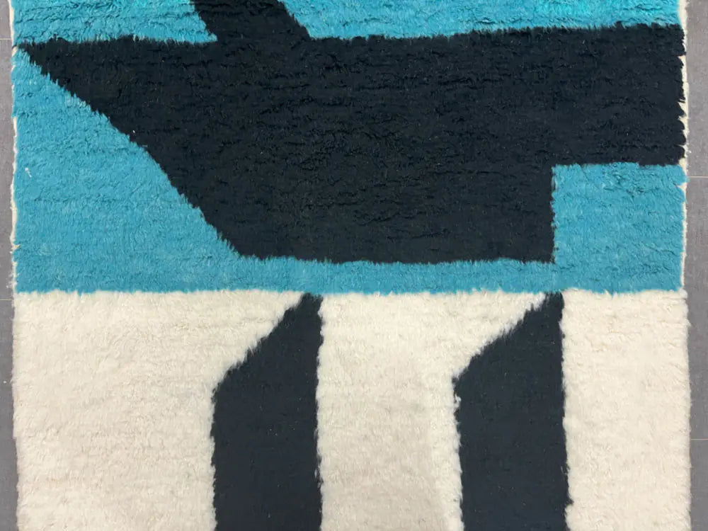 Gros plan sur un tapis berbère en laine avec motifs bleus et noirs, texture douce et épaisse.