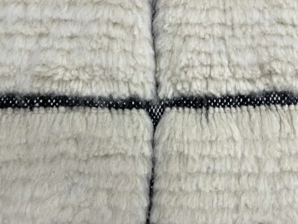 Gros plan sur la laine douce d’un tapis Blanc Beni Ouarain, qualité artisanale berbère, idéal pour intérieur chaleureux.
