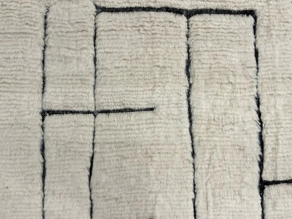 Tapis Blanc Beni Ouarain en laine naturelle avec motifs géométriques noirs, fait main au Maroc, parfait pour salon moderne.