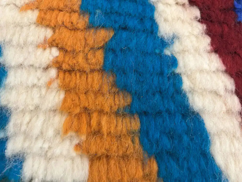 Zoom sur la texture en laine épaisse d’un tapis Azilal orange, bleu et blanc